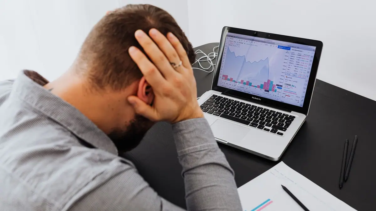 Homem estressado diante de um notebook com gráficos em queda