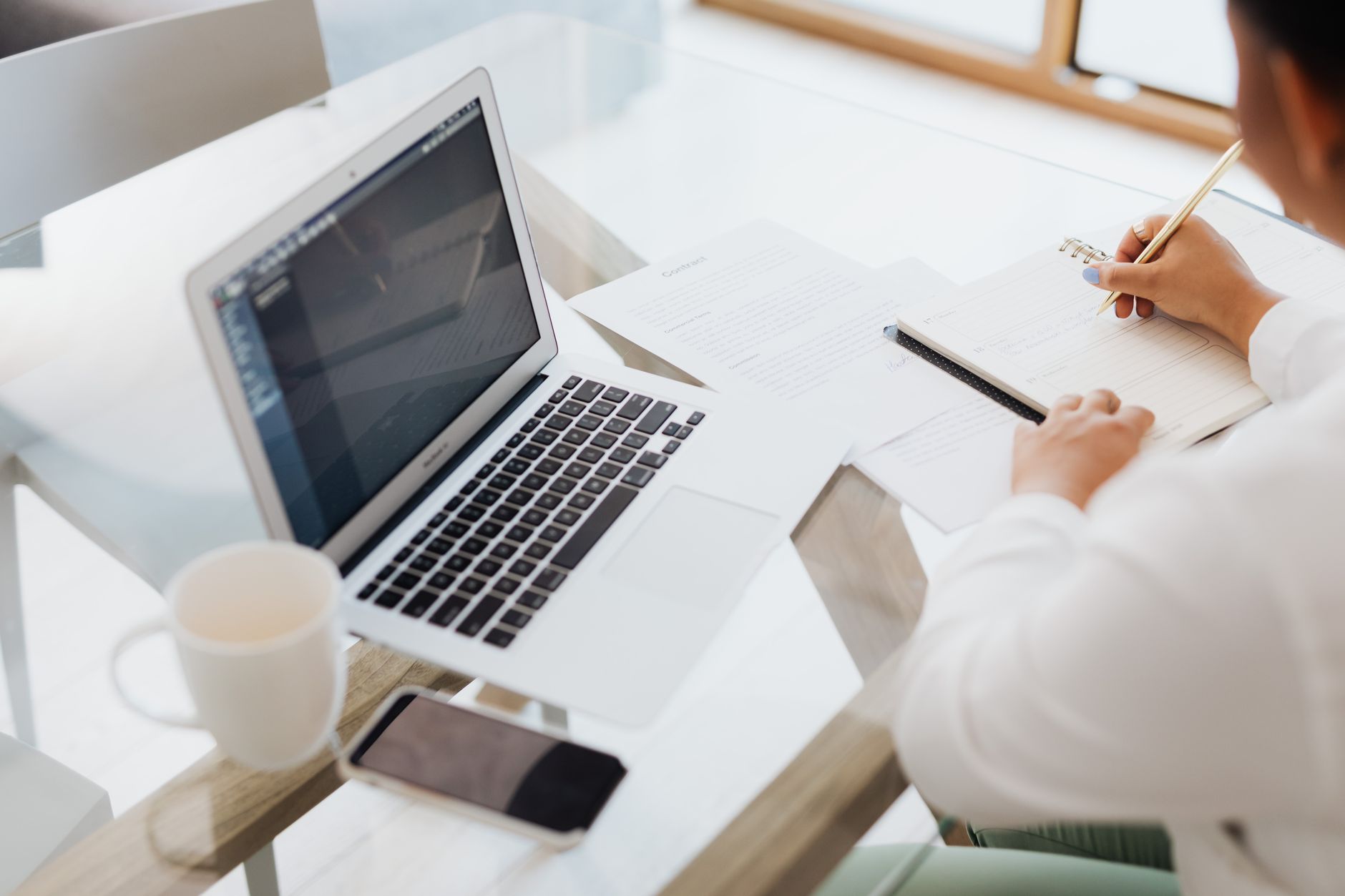 Pessoa trabalhando em casa com notebook e documentos digitais na mesa
