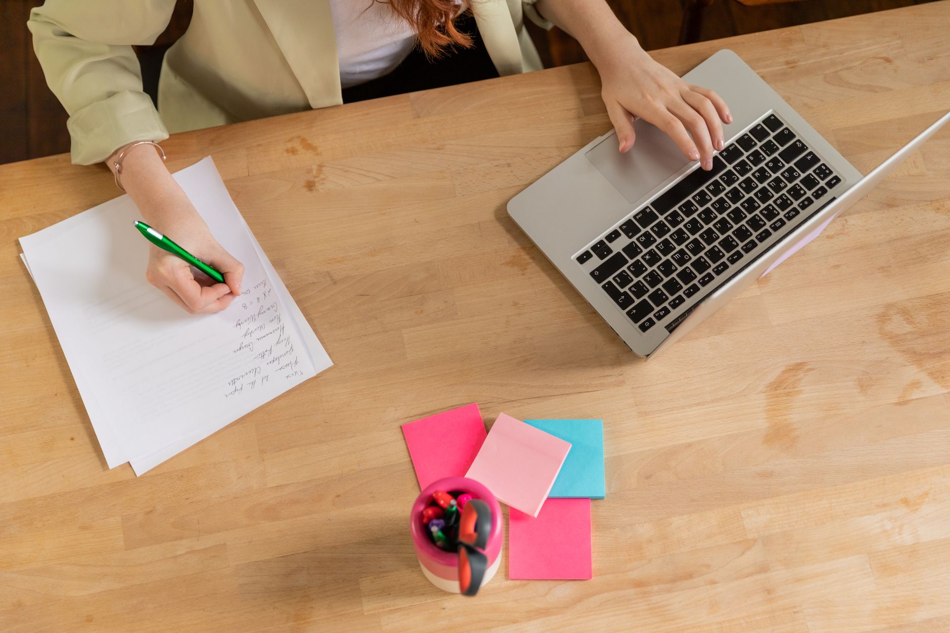 Pessoa trabalhando em um laptop com páginas organizadas em uma mesa de home office