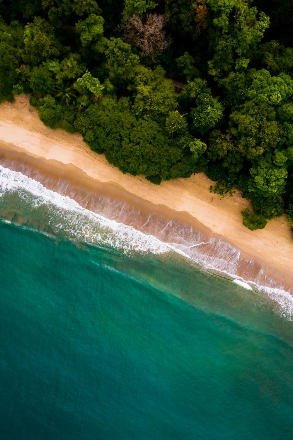 Aerial view of ocean with turquoise water, white waves, and a sandy beach.