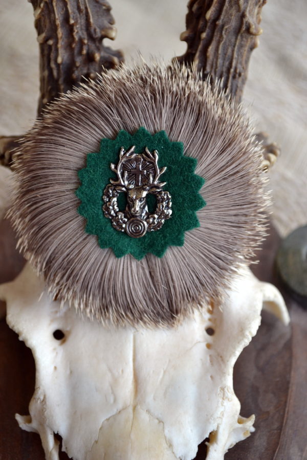 Round hat pin with badger hair wreath and cast metal deer motif at centre.