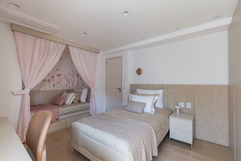 Para a mais jovem, o dormitório foi idealizado com um cantinho especial que oculta uma segunda cama através de cortinas. Esse espaço pode ser usado para descanso, leitura, receber visitas e conta com papel de parede floral para dar um toque a mais de graciosidade. | Projeto: arquiteta Daniela Funari | FOTO: Mariana Camargo