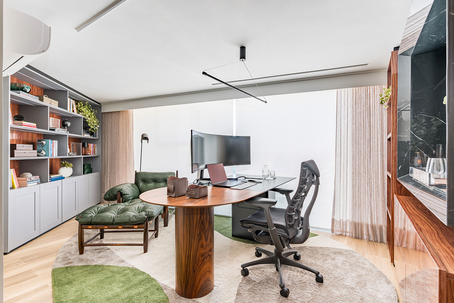 Com seus tons verdes e amadeirados e o design assinado da poltrona, este home office estruturado pela arquiteta Ana Rozenblit se beneficia da luz natural que adentra pelas amplas esquadrias | Projeto Spaço Interior | Foto: Kadu Lopes